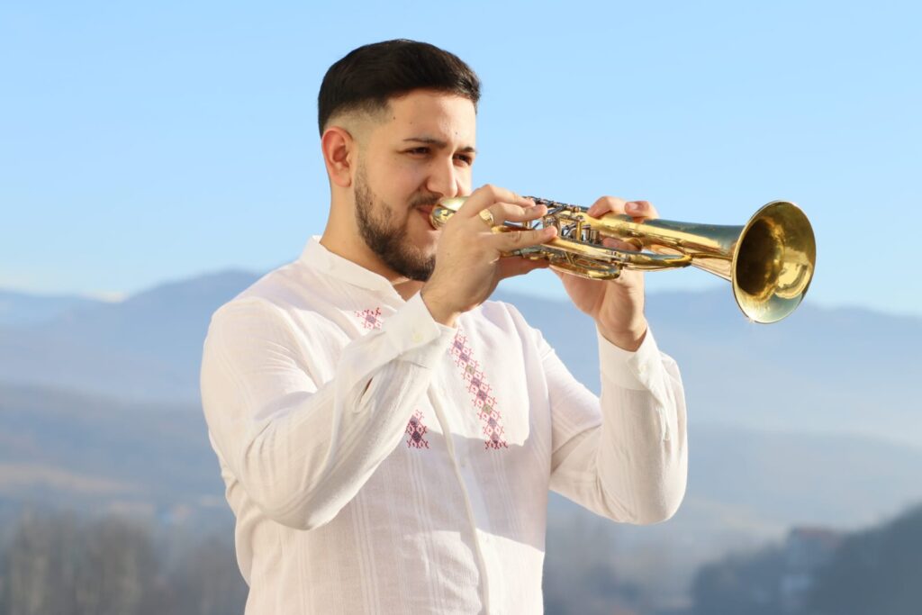 Trubač iz Orkestra AS svira na otvorenom s prelepim pejzažem u pozadini
